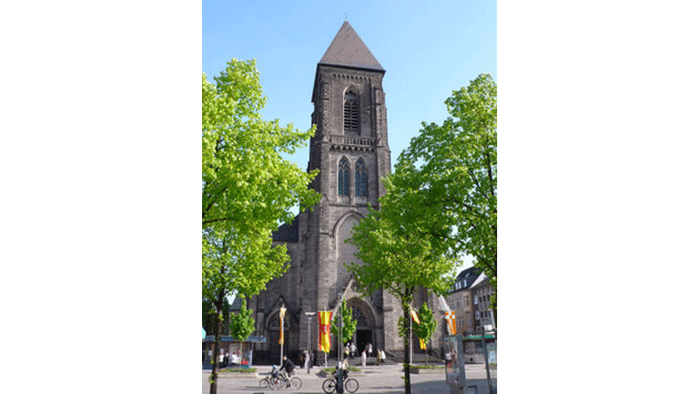 Kirche mit hohem Turm und Menschen, die Fahrrad fahren.