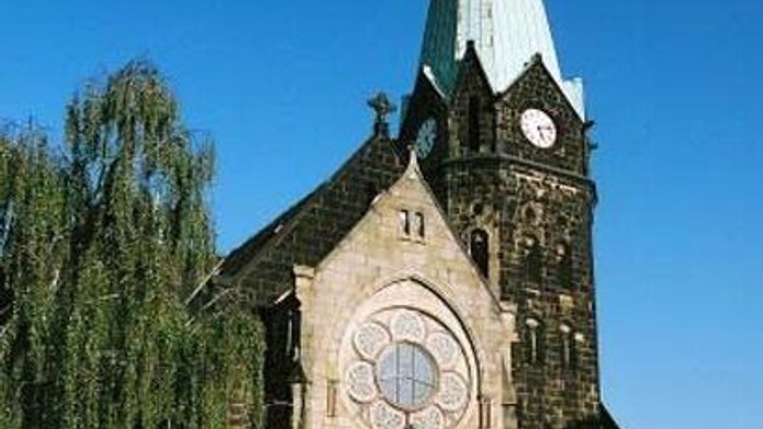 Gotische Kirche mit hohem Turm, rundem Buntglasfenster und Uhrturm vor klarem Himmel.