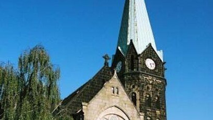 Gotische Kirche mit hohem Turm, rundem Buntglasfenster und Uhrturm vor klarem Himmel.