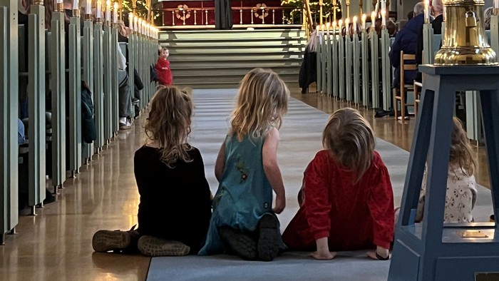 Tre børn sidder i en kirke.