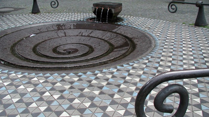 Ein runde Metallgitter liegt auf einem gefliesten Boden mit Spiralmuster.