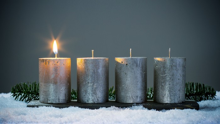 Vier Kerzen auf einem Adventsgesteck, eine davon brennt - es ist der erste Advent