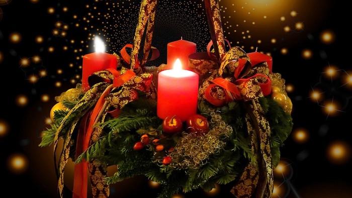 En hængende juledekorasjon med tre lysende røde lys og grønne blomster.