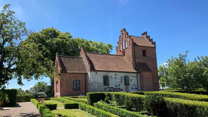 Et rødt teglmurstenshus med tårn og omgivet af en managtaget have