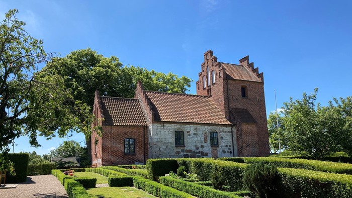 Et rødt teglmurstenshus med tårn og omgivet af en managtaget have