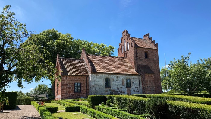 Et rødt teglmurstenshus med tårn og omgivet af en managtaget have