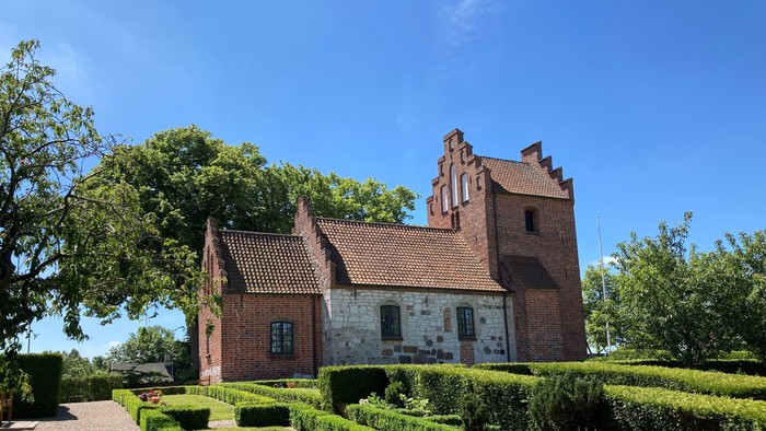 Et rødt teglmurstenshus med tårn og omgivet af en managtaget have