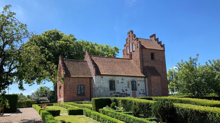 Et rødt teglmurstenshus med tårn og omgivet af en managtaget have