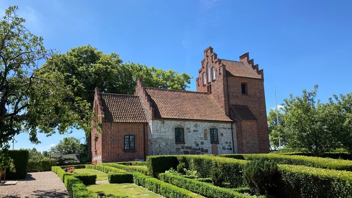 Et rødt teglmurstenshus med tårn og omgivet af en managtaget have