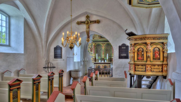 Kirkeinteriør med kirkebænke, lysekrone og udsmykket prædikestol.