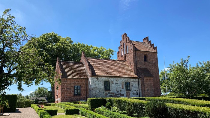 Et rødt teglmurstenshus med tårn og omgivet af en managtaget have