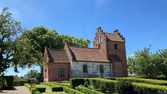 Et rødt teglmurstenshus med tårn og omgivet af en managtaget have