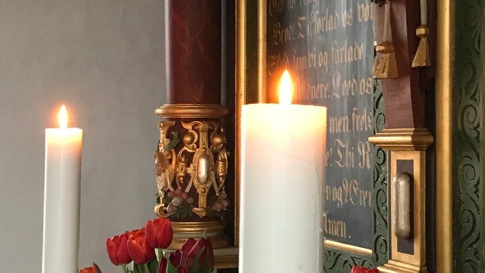 To candler, to blomsterarrangementer og en altertavle