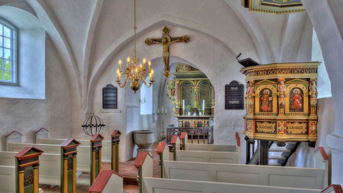 Kirkeinteriør med kirkebænke, lysekrone og udsmykket prædikestol.