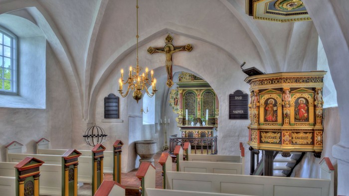 Kirkeinteriør med kirkebænke, lysekrone og udsmykket prædikestol.