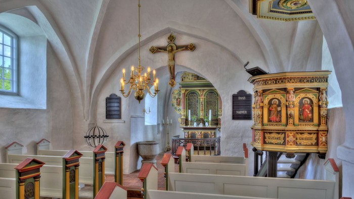 Kirkeinteriør med kirkebænke, lysekrone og udsmykket prædikestol.