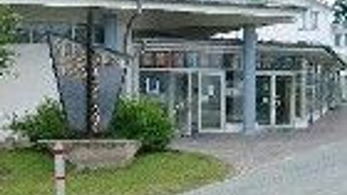 Ein Gebäude mit mehreren Fenstern und einem Schild, daneben ein Baum und ein Parkplatz.