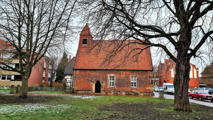 Ein altes Backsteingebäude mit rotem Dach und nackten Bäumen im Vordergrund