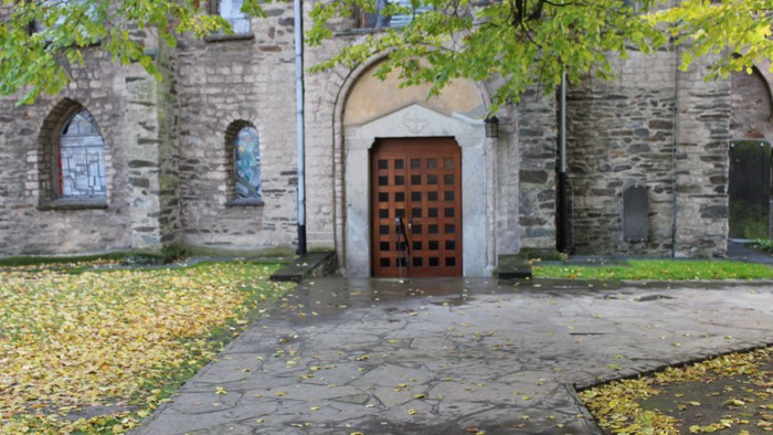 Alte Steinmauer mit Torbogen und Holzverschlag, umgeben von Bäumen und herabgefallenen Blättern