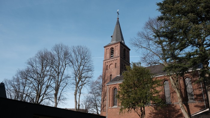 Kirchturm aus rotem Backstein vor klarem Himmel und Bäumen