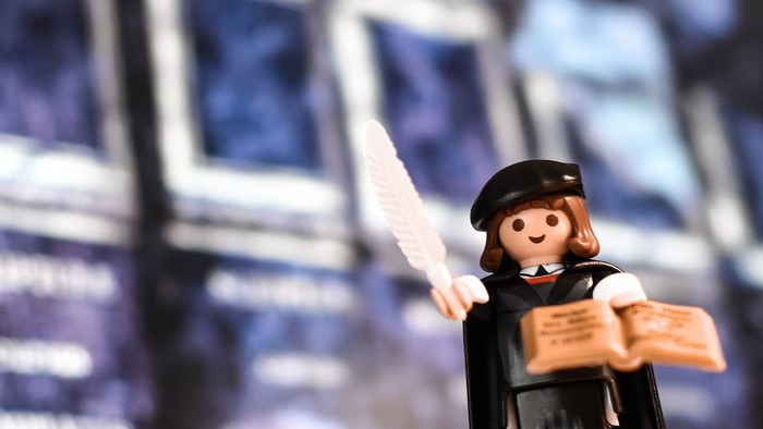 Eine Spielzeugfigur in Doktorrobe hält ein Pergament und eine Feder.