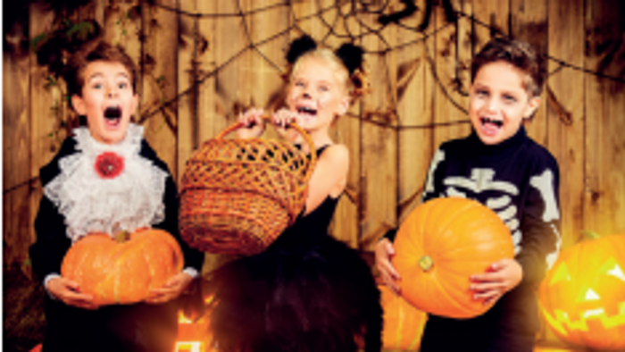 Tre børn står sammen med halloween-tromler og en pumpa.