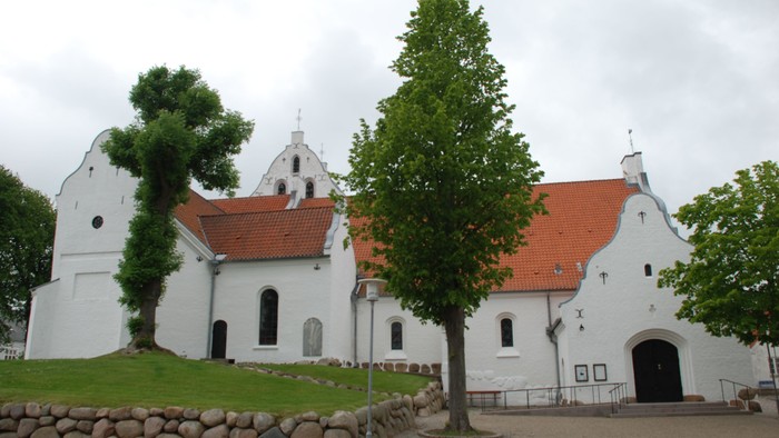 Et hvidt kirkekompleks med røde tag og grønne træer