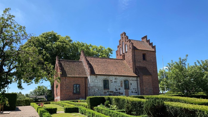 Et rødt teglmurstenshus med tårn og omgivet af en managtaget have