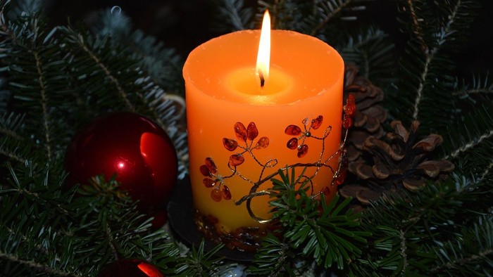 Eine brennende Kerze mit Herbstblättern, umgeben von Tannenzweigen und Weihnachtskugeln