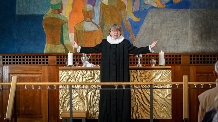 En præst står ved alteret i en kirke og holder to lysestager op.