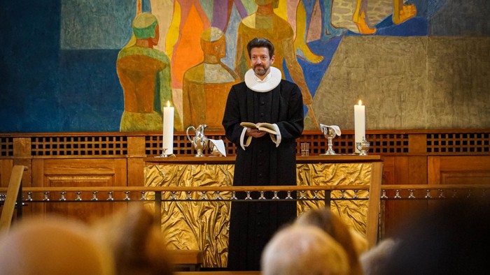 En mand i kaplan dragt står ved alteret og holder en bog.