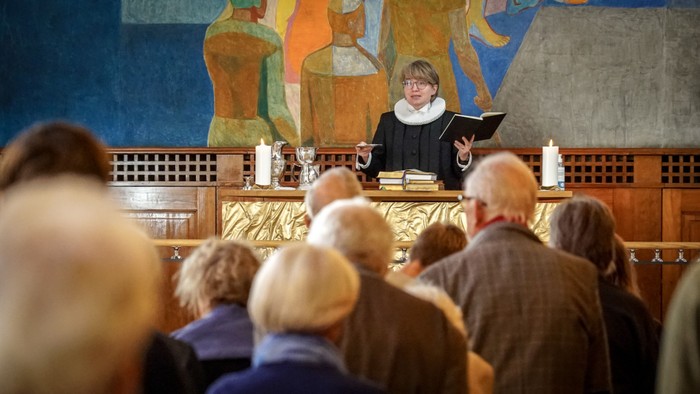 En præst holder en prædiken i en kirke med en malet altertavle bagud.