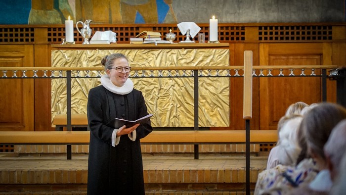 En præst i svart drøm og hvid krage står ved alteret og læser fra en bog.