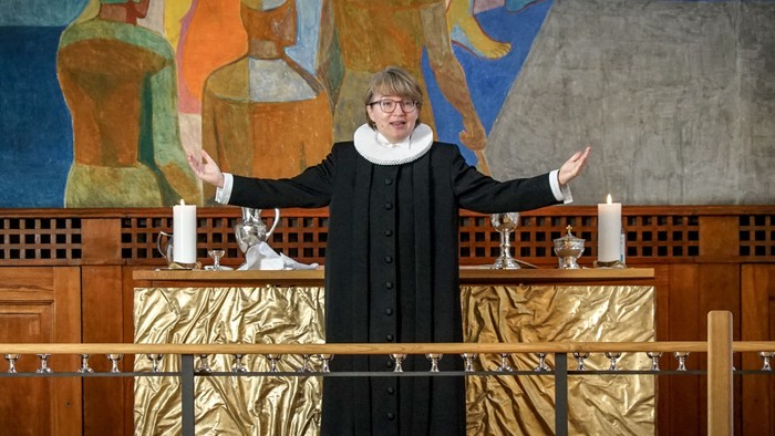 En præst står ved alteret i en kirke og holder to lysestager op.