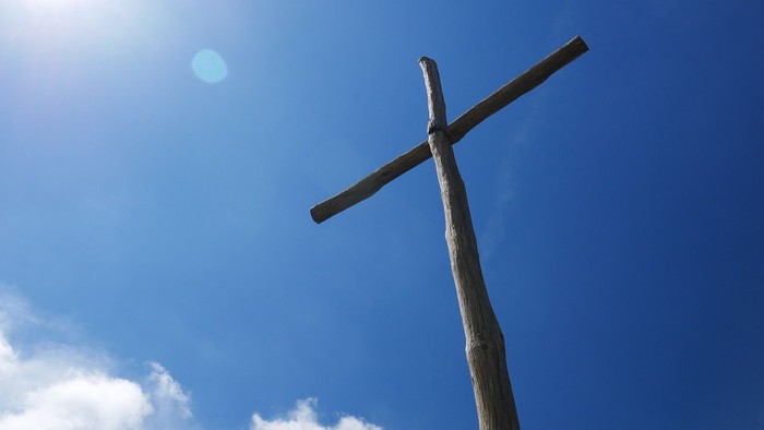 En stor korsformet struktur mod en klar blå himmel med sol og skyer.