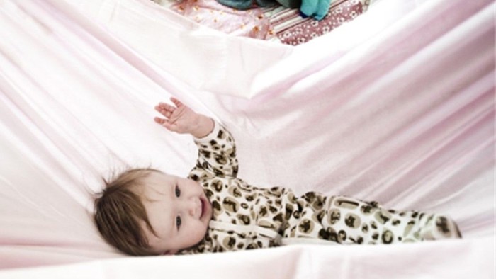 Et spæd barn ligger i en hvid og rosa babystue med legetøj.