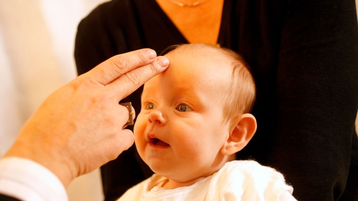 En person holder et barns hoved, mens et andet person taster barnets pande.