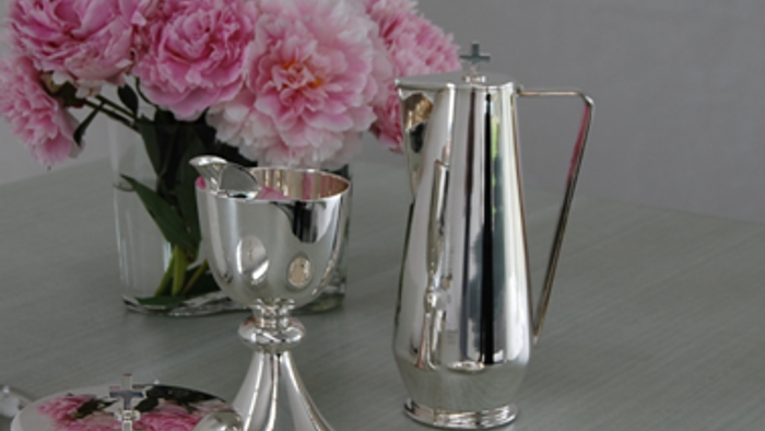 En sølv tekanne og tegnabod med rosa blomster i en vase på bordet