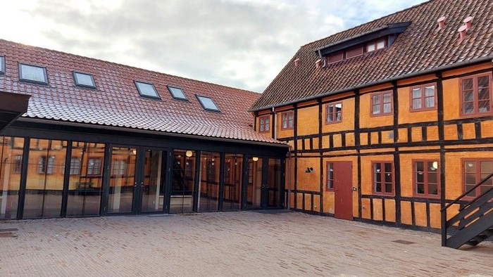 Traditionelle bindingsværkshuse med en moderne glaspavillon som indgang i en gårdhave.