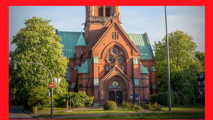 Das Bild zeigt eine rote Kirche mit grünen Dächern und einem Uhrturm.