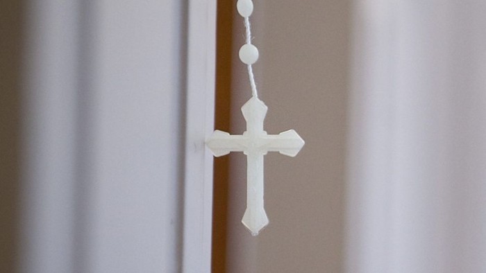 Ein weißes Kreuz hängt an einer Perlenkette an einer Tür.