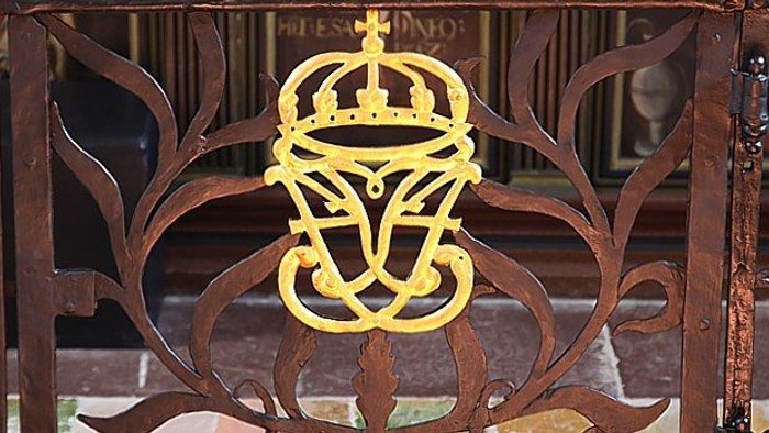 En smedejernsgitter med et gult kronede monogramm.