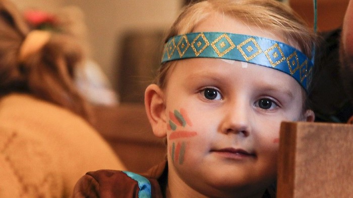 Et barn med blå hovedbånd og malet ansigt ser efterlænge.