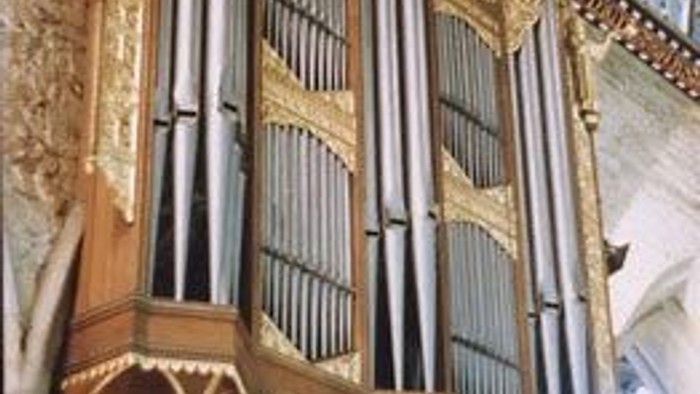 Ornate pipe organ with gold accents in a grand hall.