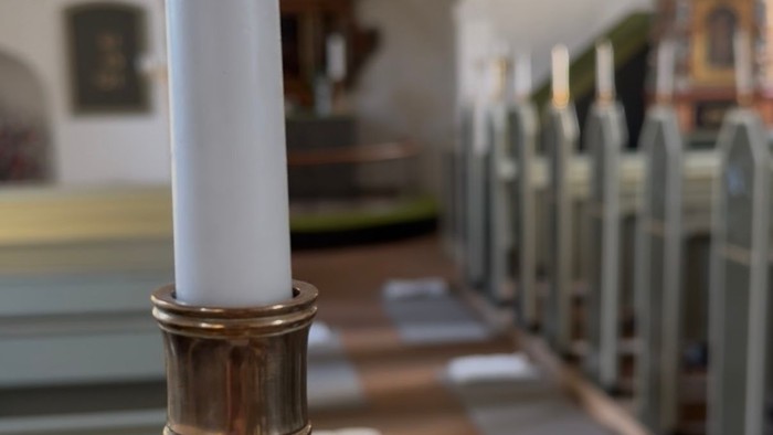Et stearinlys i en messinglysestage på et bord i en kirke.