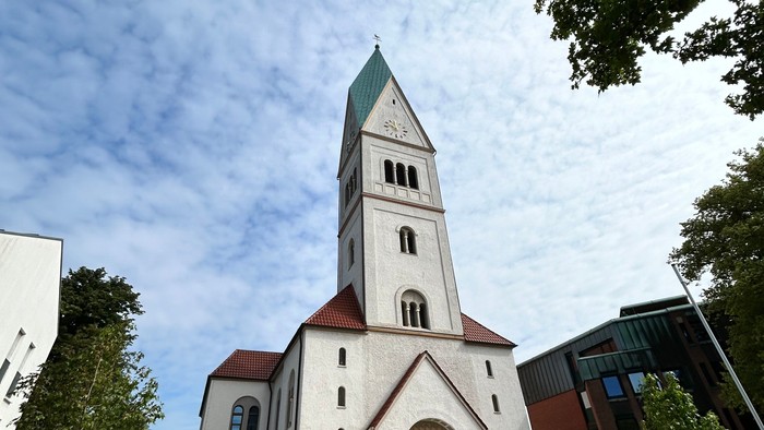 Weiße Kirche mit hohem Turm und grünem Dach vor blauem Himmel