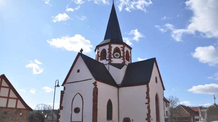 Eine charmante Kirche mit einem hohen Kirchturm und traditionellem architektonischem Design vor einem strahlend blauen Himmel.