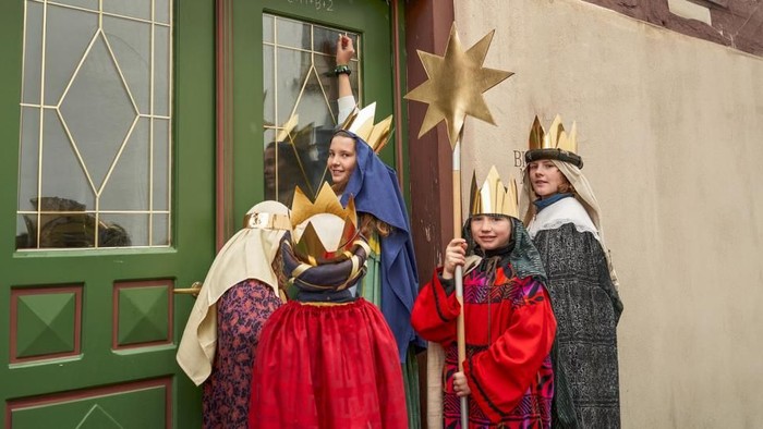 Vier Personen in farbenfrohen Gewändern und Kronen stehen vor einer grünen Tür, zwei halten Sterne.