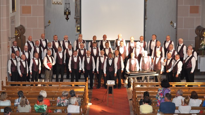 Ein formeller Chorauftritt in einer Kirche mit Publikum, das in Bänken sitzt und aufeinander abgestimmte Kleidung trägt.