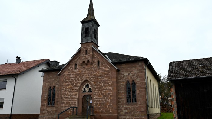 Historische Steinkirche mit spitzem Turm und Bogenfenstern, gelegen in einer ruhigen Wohngegend.
